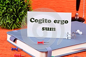 The words Cogito Ergo Sum or I think Therefore I Am on a white business card standing on a notepad