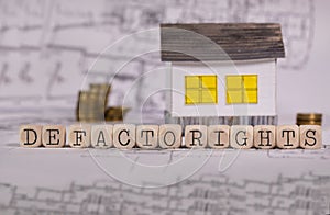 Words DE FACTO RIGHTS composed of wooden letter. Small paper house in the background