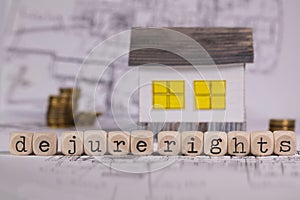 Words DE JURE RIGHTS composed of wooden letter. Small paper house in the background