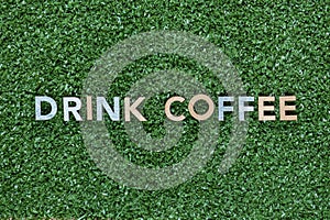 The words Drink coffee made from multicolored letters on grass background, shot from above, aligned in the center