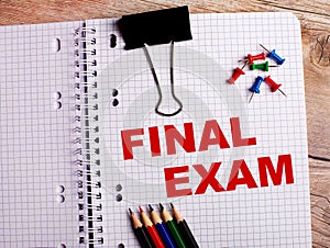 The words FINAL EXAM is written in a notebook near multi-colored pencils and buttons on a wooden background