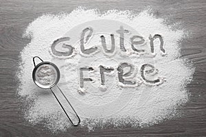 Words Gluten free written with flour and metal strainer on wooden table, flat lay