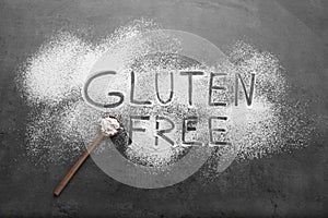 Words Gluten free written with flour and wooden spoon on grey background, flat lay