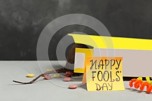 Words Happy Fool`s Day and box of corn rings with fake rat`s tail on light grey table. Space for text