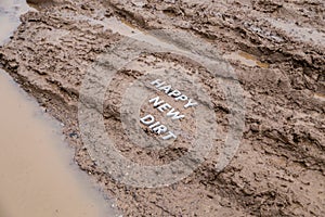 The words happy new dirt laid with silver metal letters on wet mud surface