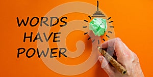 Words have power symbol. Businessman writing text `Words have power`, isolated on beautiful orange background. Light bulb icon.