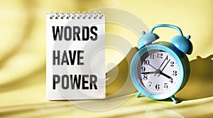 Words have power, text in a notepad on a yellow background with a clock