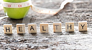 Words of Healthy concepts collected in crossword with wooden cubes. Green apple and measuring tap background.