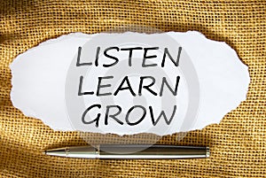 Words `Listen, learn, grow on white paper. Black metallic pen. Beautiful canvas background.