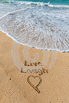 The words Live, Laugh, and a heart written in the sand on the beach
