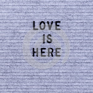 The words Love Is Here on grey felt letter board
