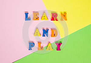 Words made of multi-colored wooden letters `learn and play` on a multi-colored background