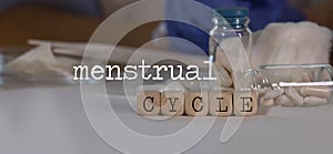 Words MENSTRUAL CYCLE composed of wooden dices. Pills, documents and a pen in the background