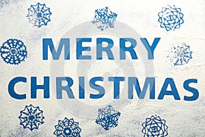 Words MERRY CHRISTMAS and snowflakes made of flour on blue background, top view