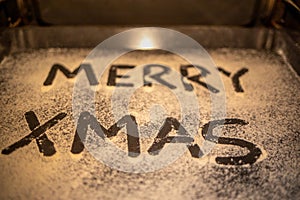 Words Merry Xmas is written on a baking tray sprinkled with powdered sugar or flour