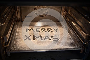 Words Merry Xmas is written on a baking tray sprinkled with powdered sugar or flour