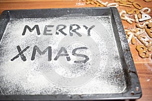 Words Merry Xmas is written on a baking tray sprinkled with powdered sugar or flour