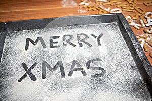 Words Merry Xmas is written on a baking tray sprinkled with powdered sugar or flour