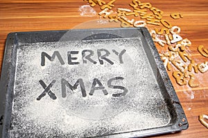 Words Merry Xmas is written on a baking tray sprinkled with powdered sugar or flour