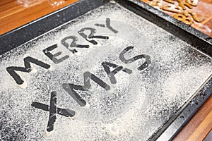 Words Merry Xmas is written on a baking tray sprinkled with powdered sugar or flour