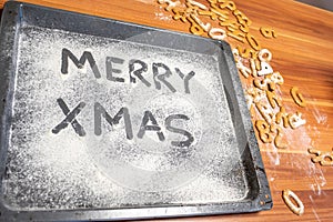 Words Merry Xmas is written on a baking tray sprinkled with powdered sugar or flour