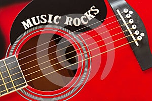 Words Music Rocks with wooden letters, closeup on a surface of red acoustic guitar. Music entertainment background