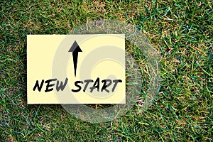 The words new start written on paper on green grass background. Inspirational quote to create a new future or beginning in