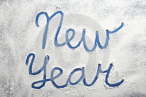 Words New Year made of flour on blue background, top view