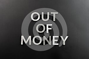 The words out of money laid with white brushed metal letters on flat black surface