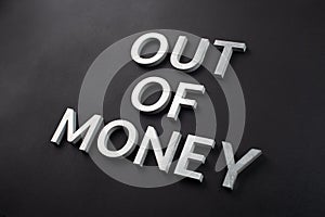 The words out of money laid with white brushed metal letters on flat black surface with diagonal composition and