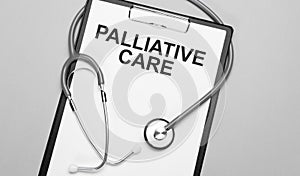 The words palliative care is written on white paper on a grey background near a stethoscope. Medical concept