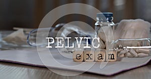 Words  PELVIC EXAM composed of wooden dices. Pills, documents and a pen in the background