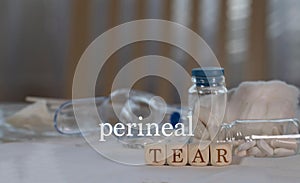 Words PERINEAL  TEAR  composed of wooden dices. Pills, documents and a pen in the background photo