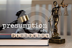 Words PRESUMPTION of PATERNITY  composed of wooden dices. Wooden gavel and statue of Themis in the background photo