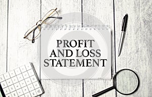 words profit and loss statement on wooden background and office supplies