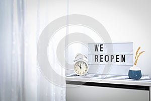 Words WE REOPEN and reopening on the light box and vintage alarm clock. New life, new business, new deals concept