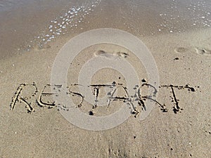 Words `Restart` written on wet sand at the sea