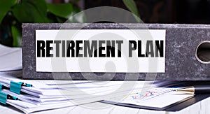 The words RETIREMENT PLAN is written on a gray file folder next to documents. Business concept