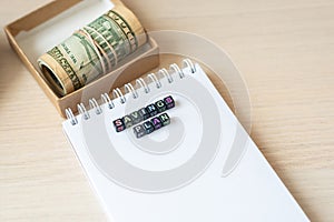 Words savings plan laid out from blocks with letters, money banknotes dollars in craft box on table