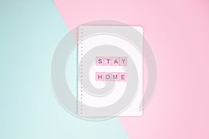 Words `stay home` made of pink wooden letters on notepad.