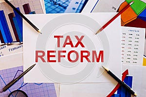 The words TAX REFORM is written on a white background near colored graphs, pens and pencils. Business concept