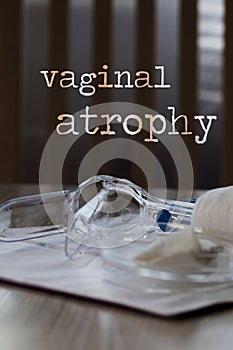 Words VAGINAL ATROPHY. Plastic vaginal speculum, pills and other tools in the background