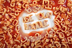 The words â€˜use your noodleâ€™ written in alphabetti spaghetti, orange pasta shaped letters