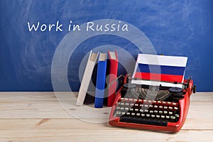 work abroad concept - red typewriter, flag of the Russia, books on table and blackboard with text & x22;Work in Russia