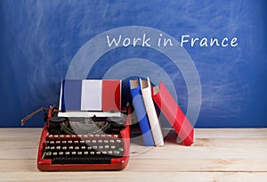 work abroad concept - typewriter, flag of the France, books on table and blackboard with text & x22;Work in France