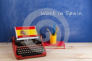 work abroad concept - typewriter, flag of Spain, books on table and blackboard with text & x22;Work in Spain