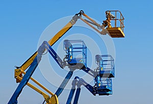 Work aerial platforms against blue cloudless sky. One cherry picker yellow among three blue