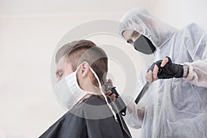 The work of the barber during the coronavirus, the hairdresser trim the client in a mask and a protective suit, quarantine