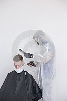 The work of the barber during the coronavirus, the hairdresser trim the client in a mask and a protective suit, quarantine