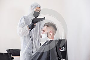 The work of the barber during the coronavirus, the hairdresser trim the client in a mask and a protective suit, quarantine